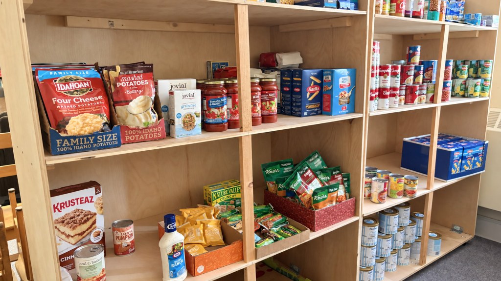 Food pantry shelves with pasta, pasta sauce, canned soups and vegetables, instant potatoes, and snacks