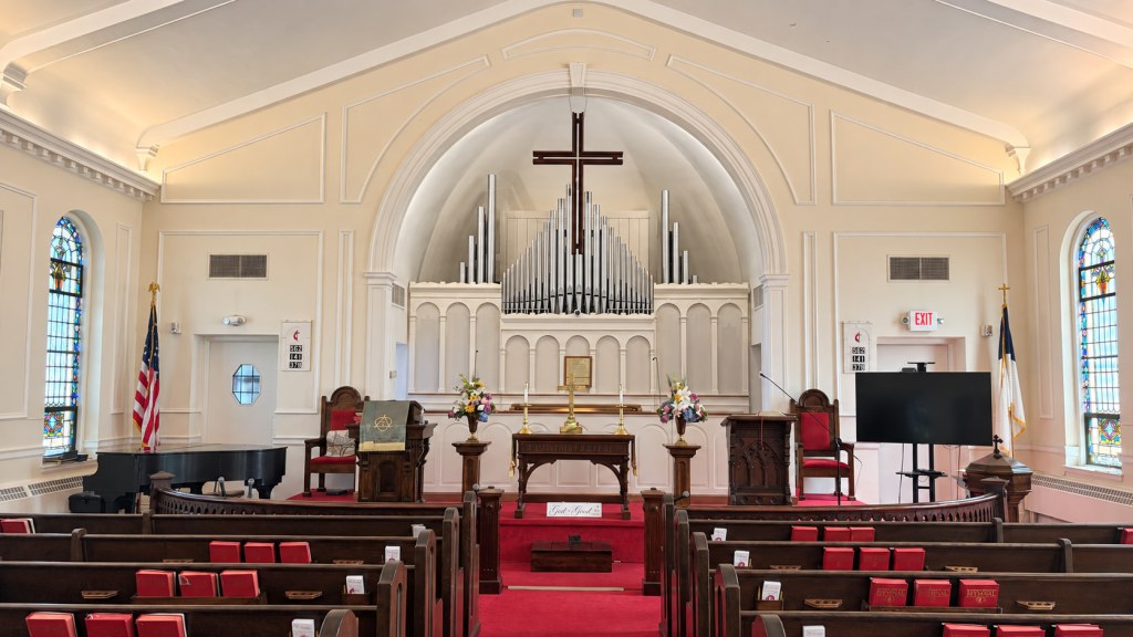 View up the center aisle to the chancel: altar table, pulpit, lectern, and a wooden cross in front of the organ pipes