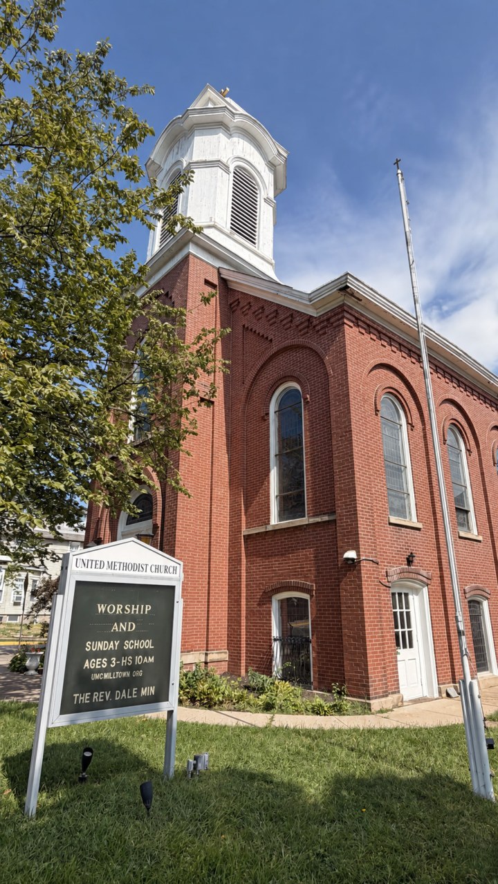 Red-brick United Methodist Church at Milltown with its white bell tower and front sign listing worship and Sunday School at 10 a.m.