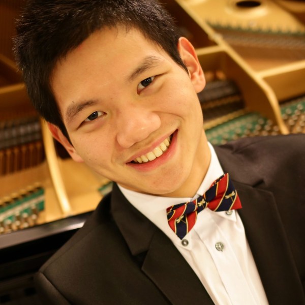 Tenson Liang, Music Director, smiling in front of an open grand piano