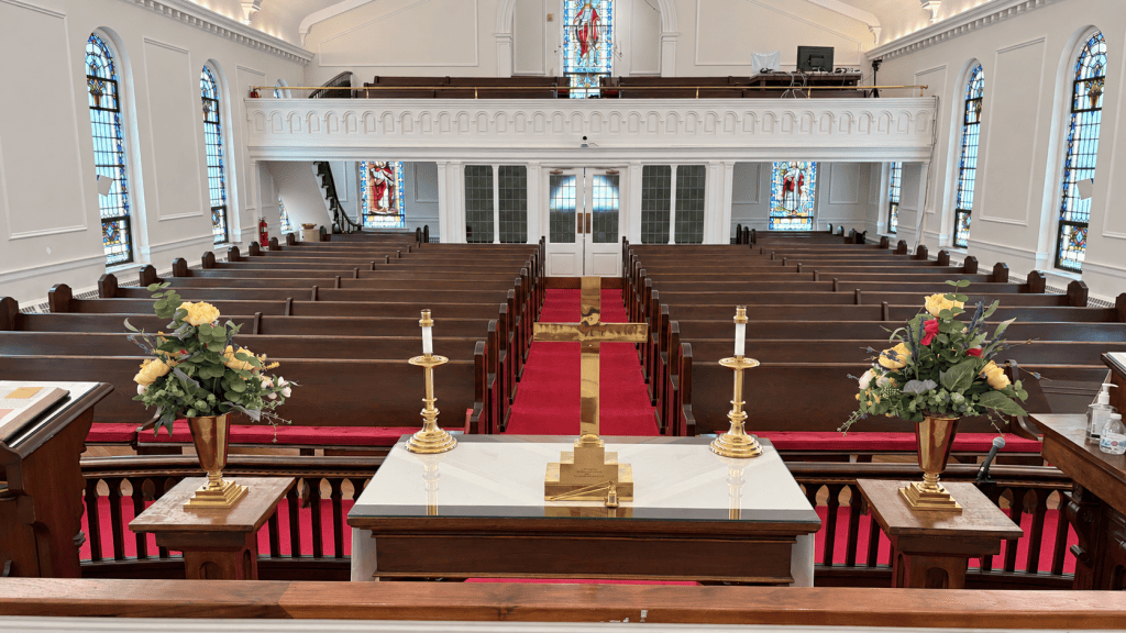 Sanctuary of the United Methodist Church at Milltown, with stained-glass windows, wooden pews, a red-carpeted aisle, and the brass altar cross